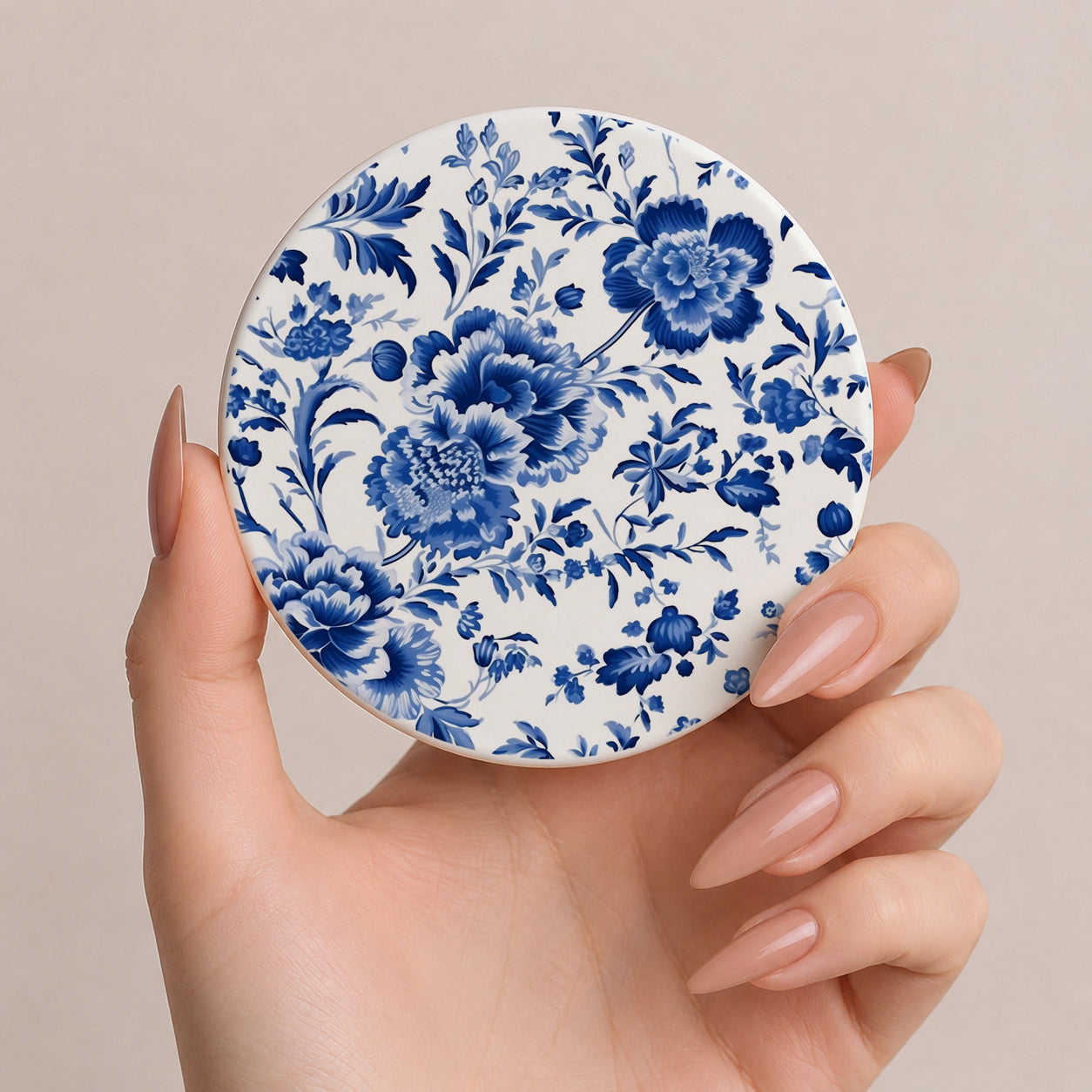 Hand holding a round ceramic coaster with blue floral pattern on a beige background