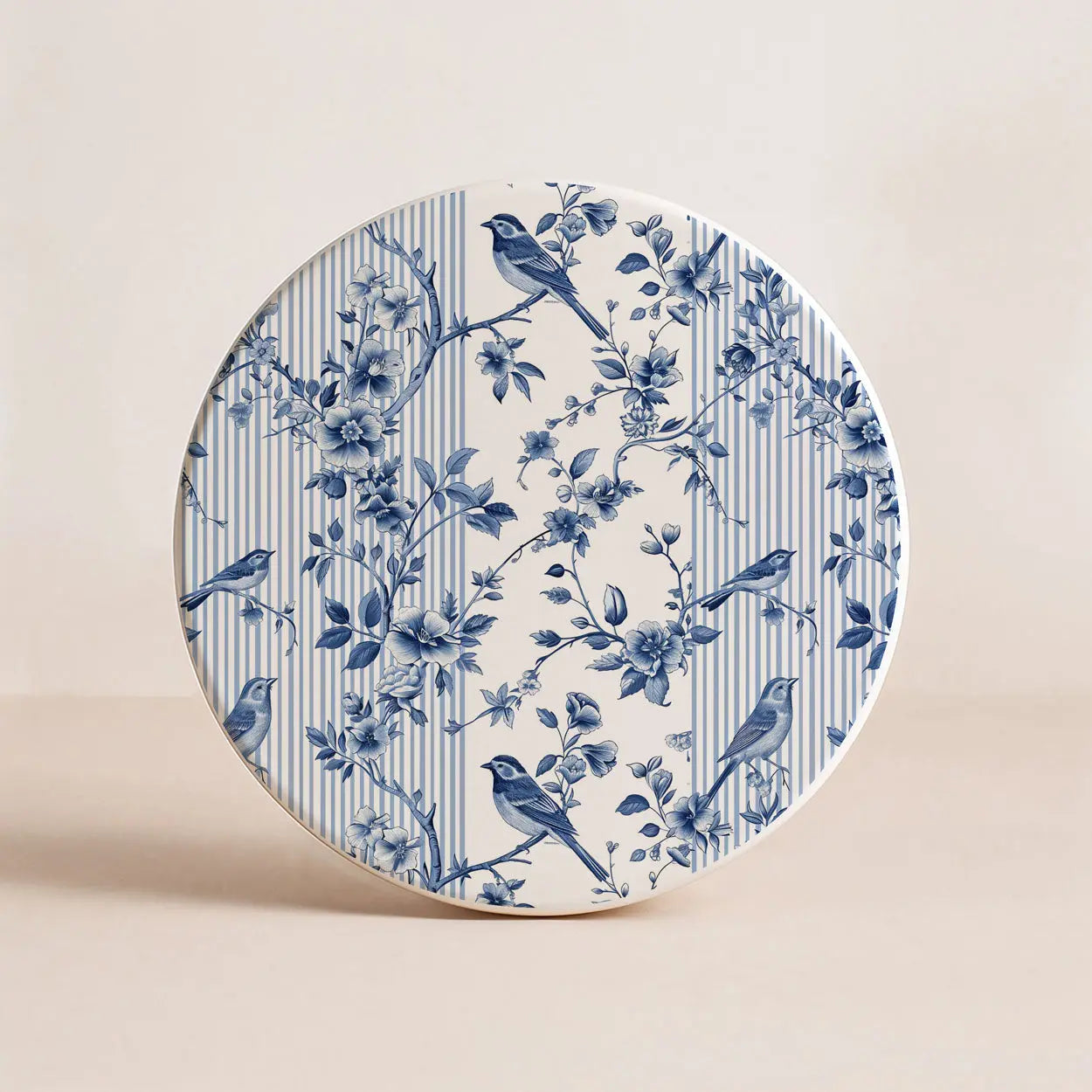 Round ceramic coaster with blue floral and bird pattern on a beige background