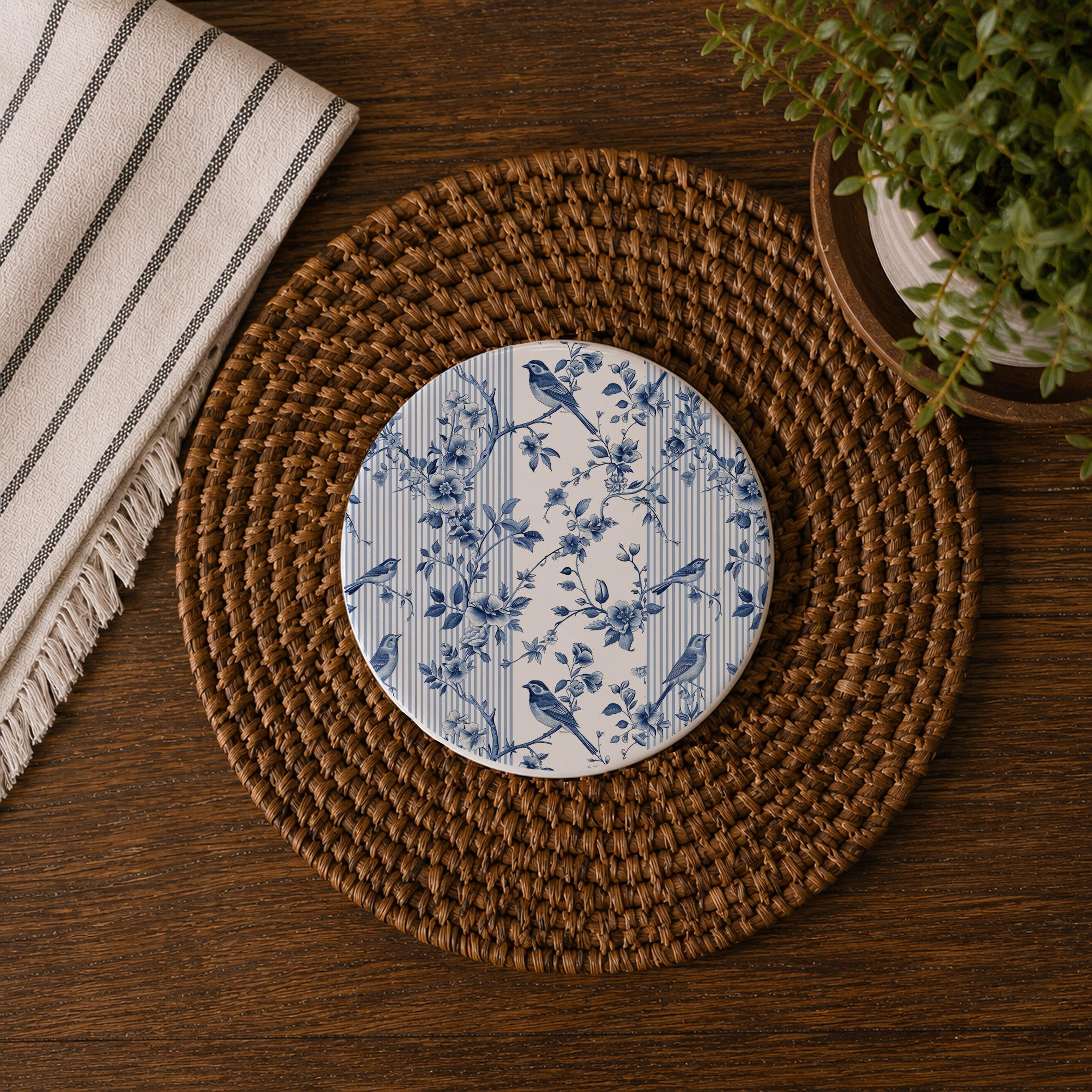 Round ceramic coaster with blue floral and bird pattern on a woven placemat