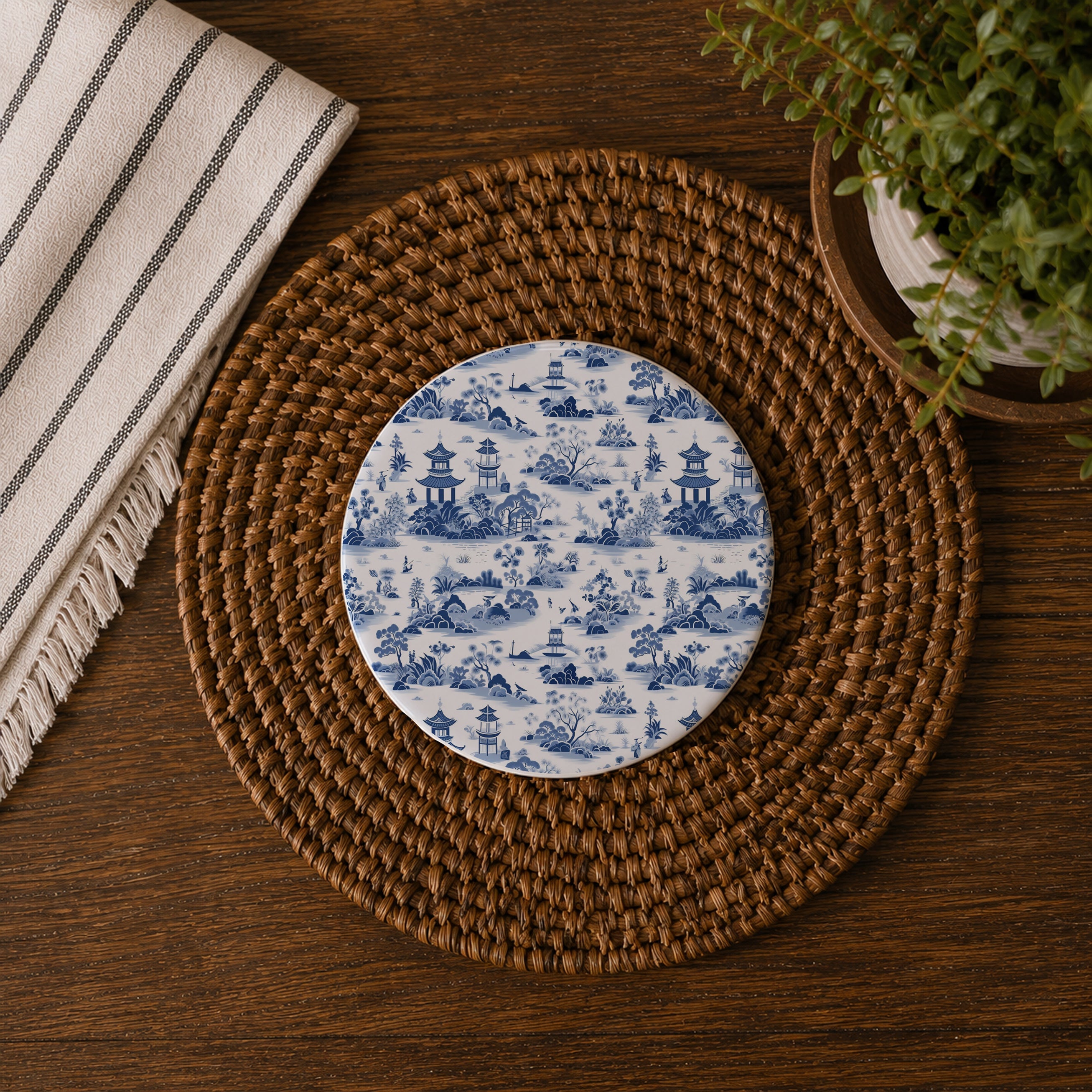 Round blue and white patterned coaster on a woven placemat with a plant and towel in the background.