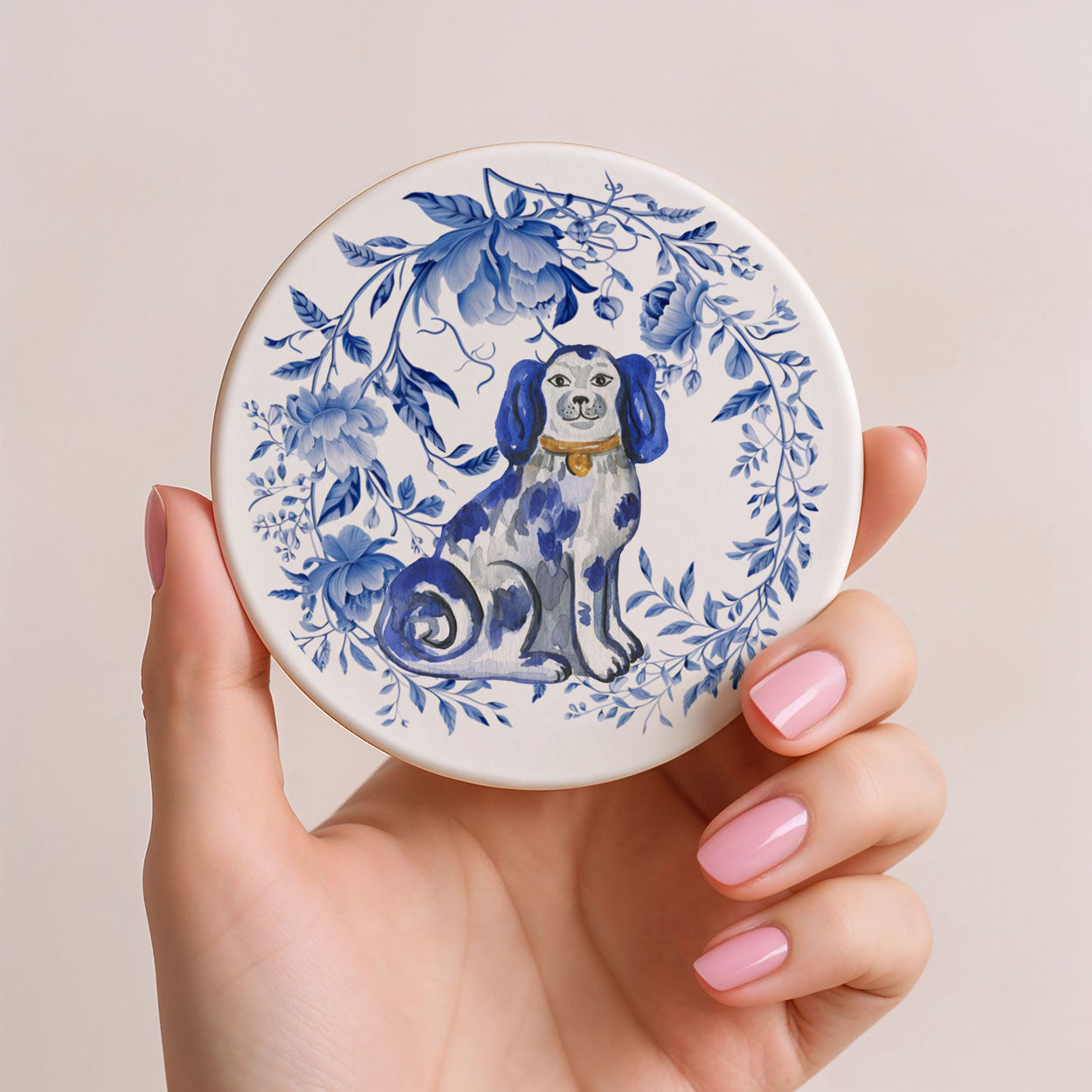 Hand holding a round ceramic coaster with a blue and white dog design on a beige background