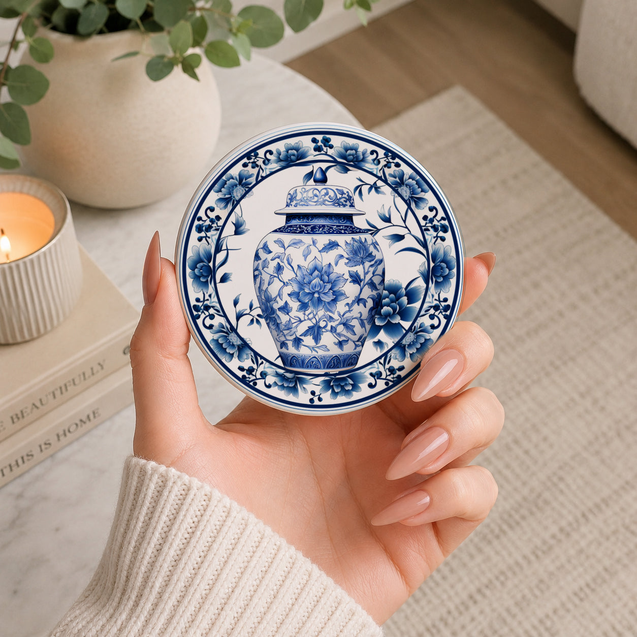 Hand holding a blue and white decorative ceramic coaster with floral patterns, blurred indoor settings