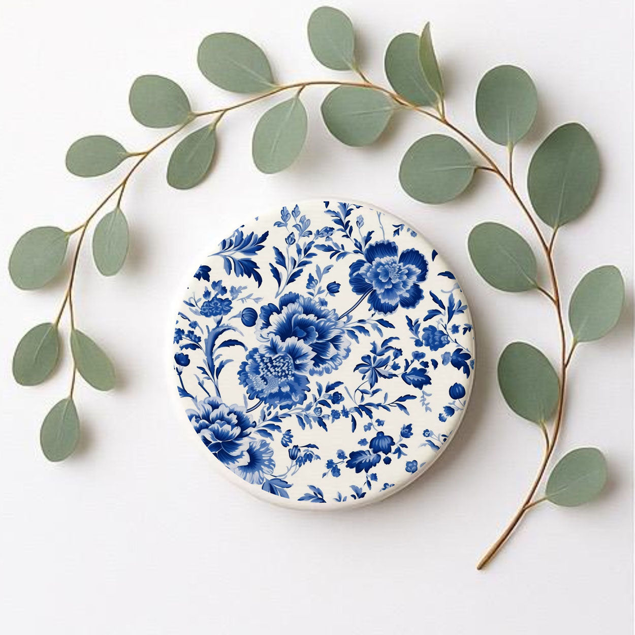 Decorative coaster with blue floral pattern surrounded by green leaves on a white background