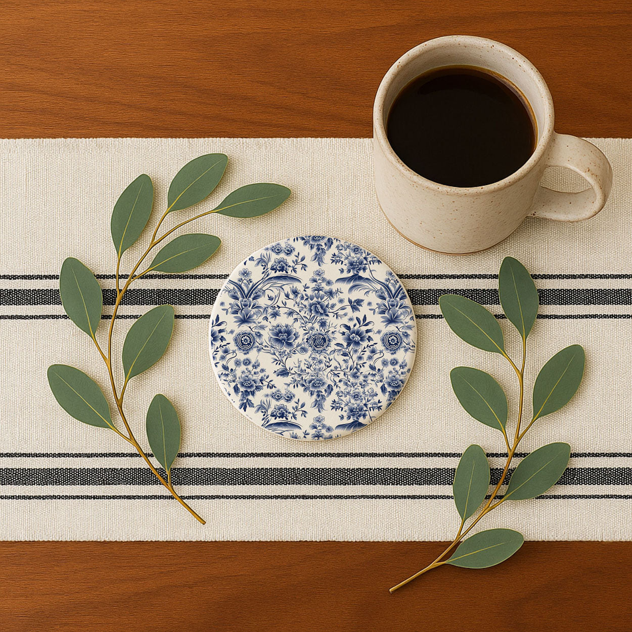 Cup of coffee on a striped placemat with a decorative coaster and green leaves.
