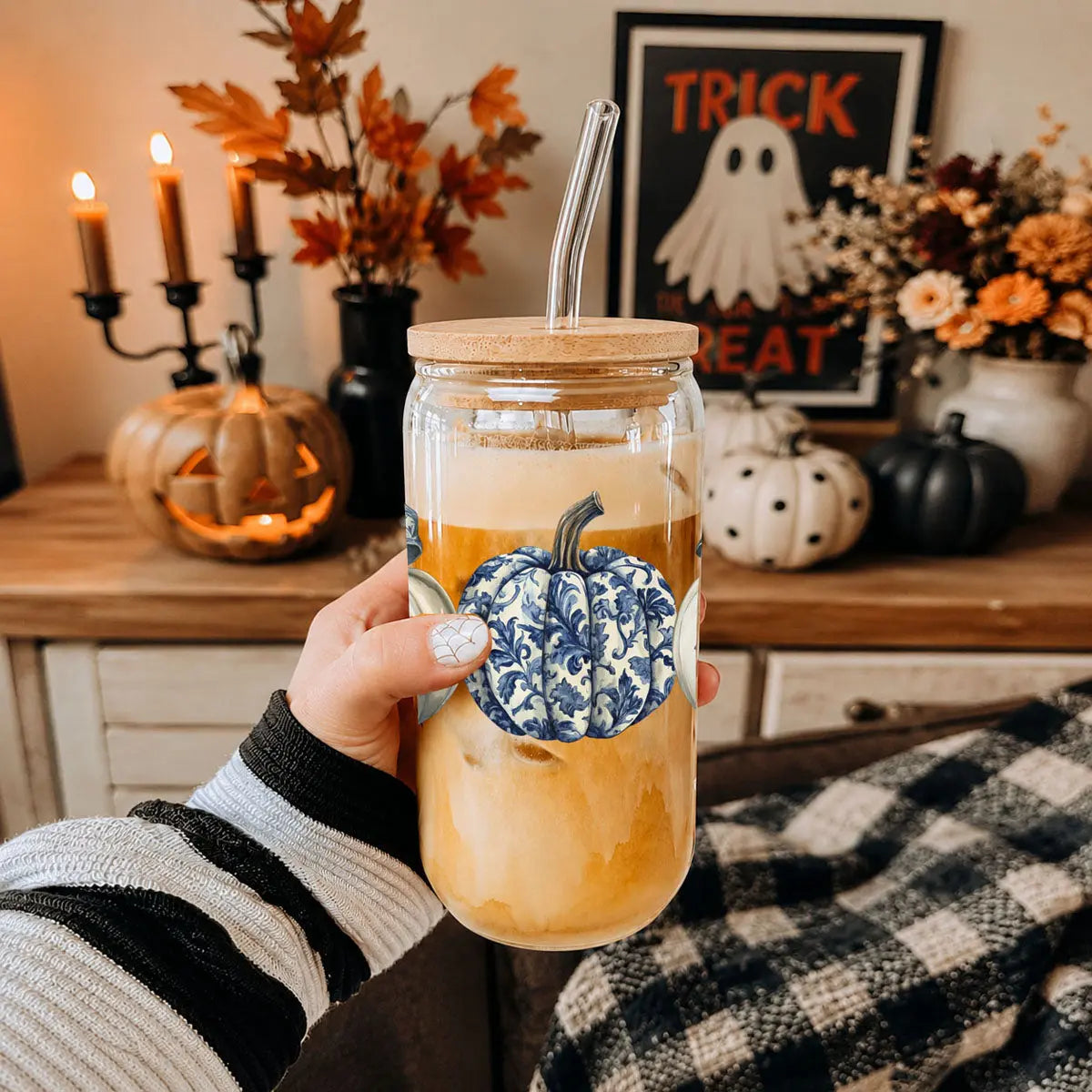 Person holding a mason jar with a floral pumpkin design, surrounded by Halloween decorations.