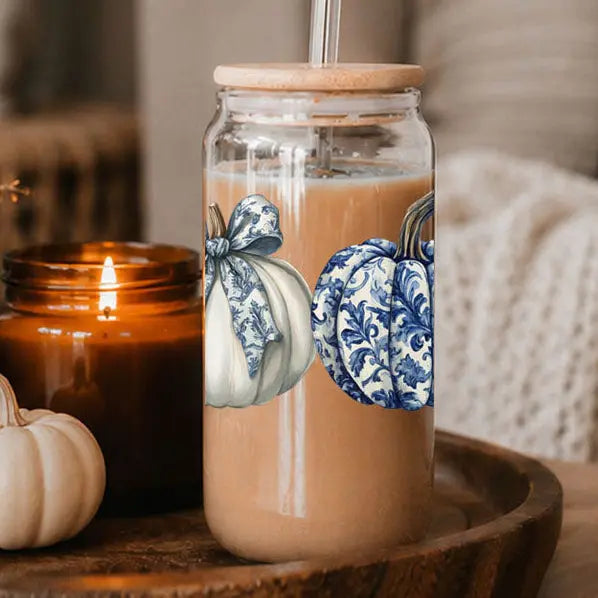 Glass jar with a wooden lid containing a beverage, surrounded by pumpkins and a candle on a wooden surface.