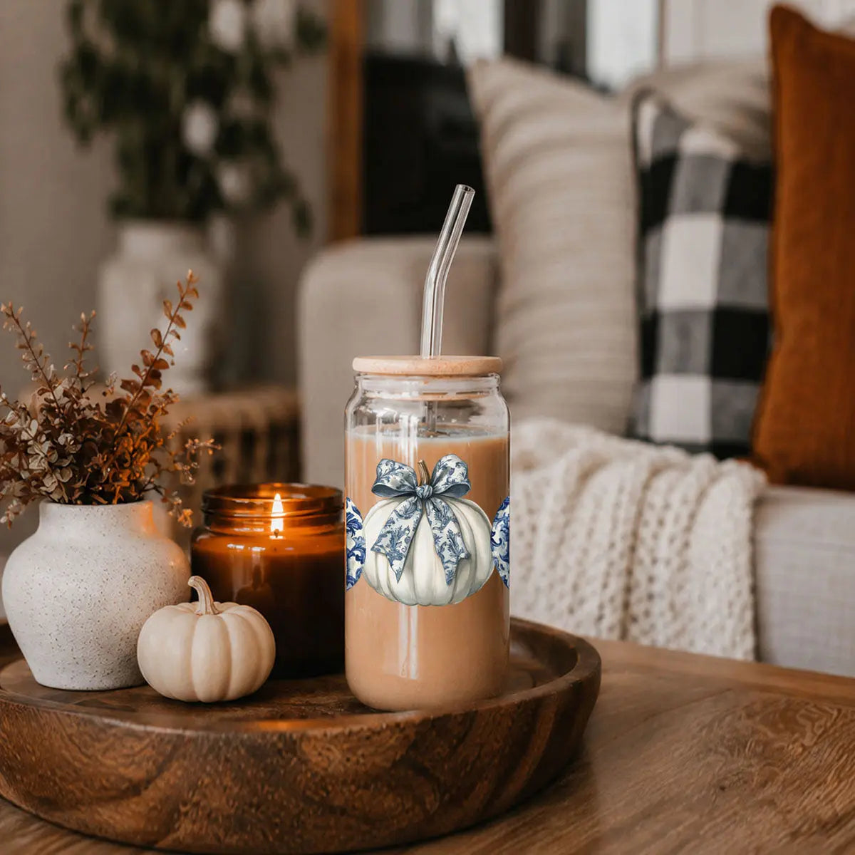 Mason jar with pumpkin design on a wooden tray with a candle and decorative items.