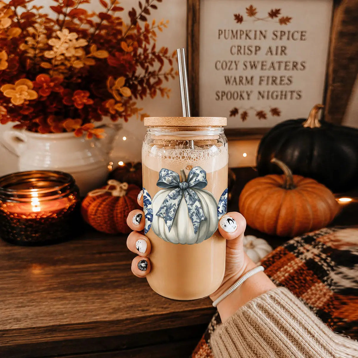 Hand holding a mason jar with pumpkin spice latte, surrounded by autumn decorations.