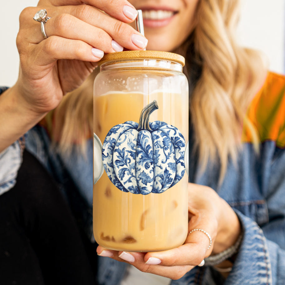 Person holding a glass jar with a blue and white pumpkin design on a white background