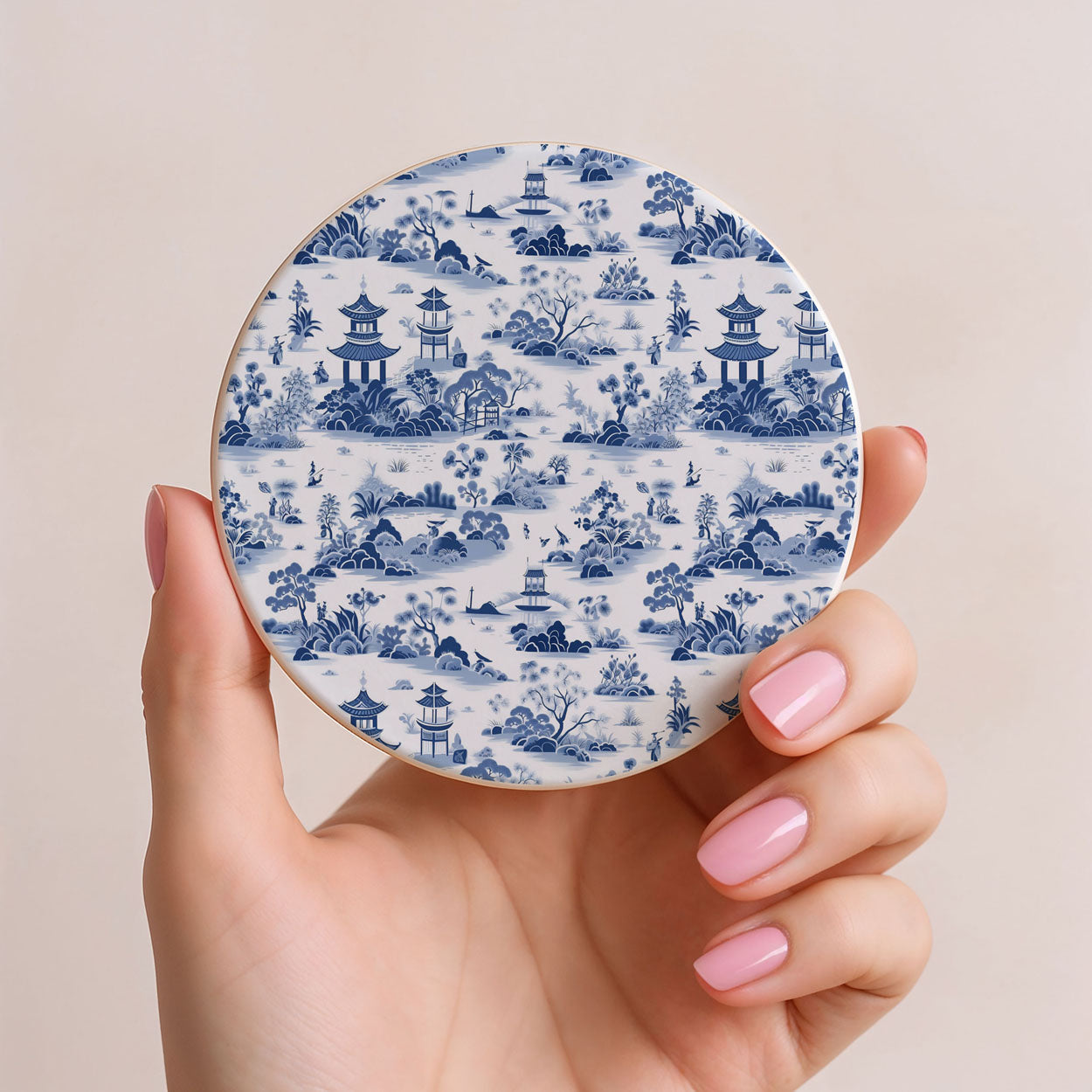Hand holding a round coaster with blue and white pattern on a beige background