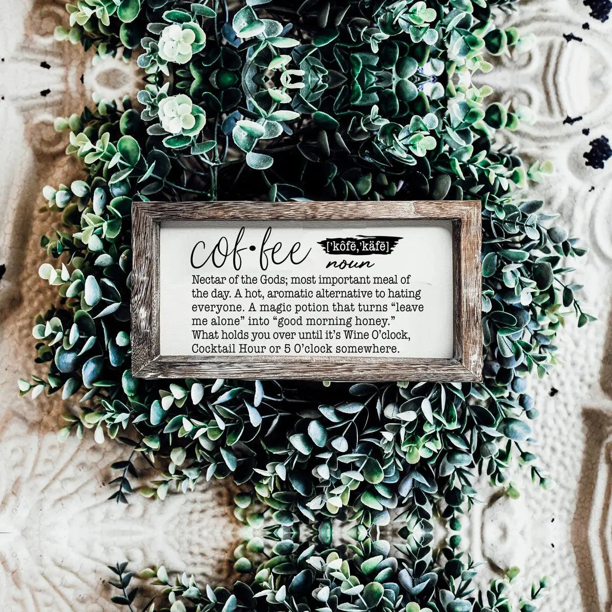 Decorative sign with coffee definition surrounded by greenery on a textured background