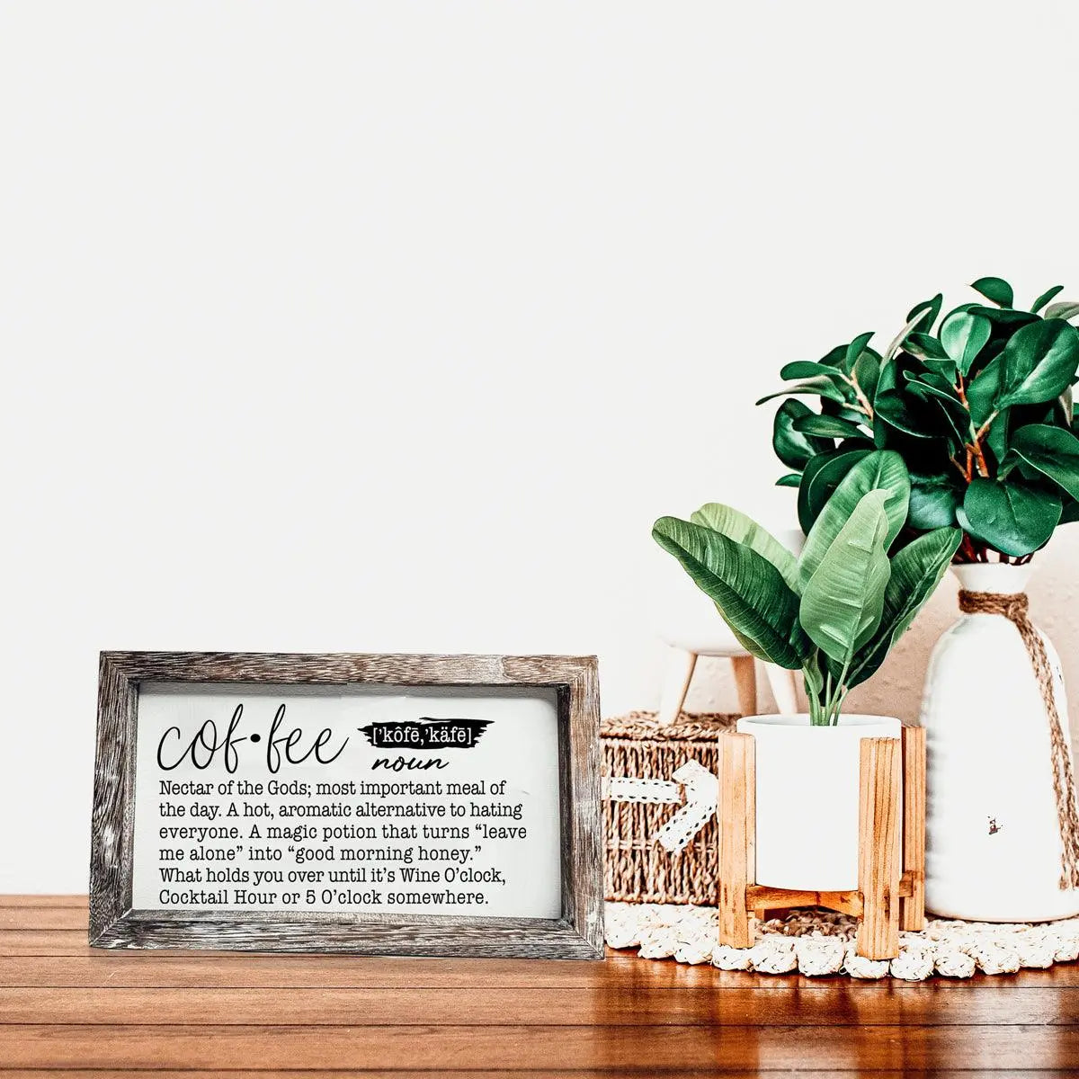Decorative sign with coffee definition on a wooden surface with plants and decor items.