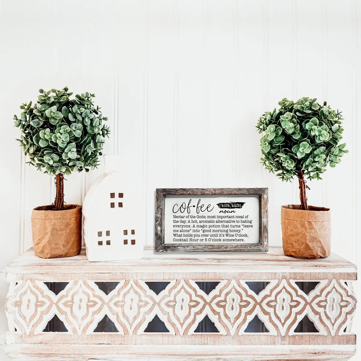 Decorative shelf with two potted plants, a small house, and a framed picture on a white wall.