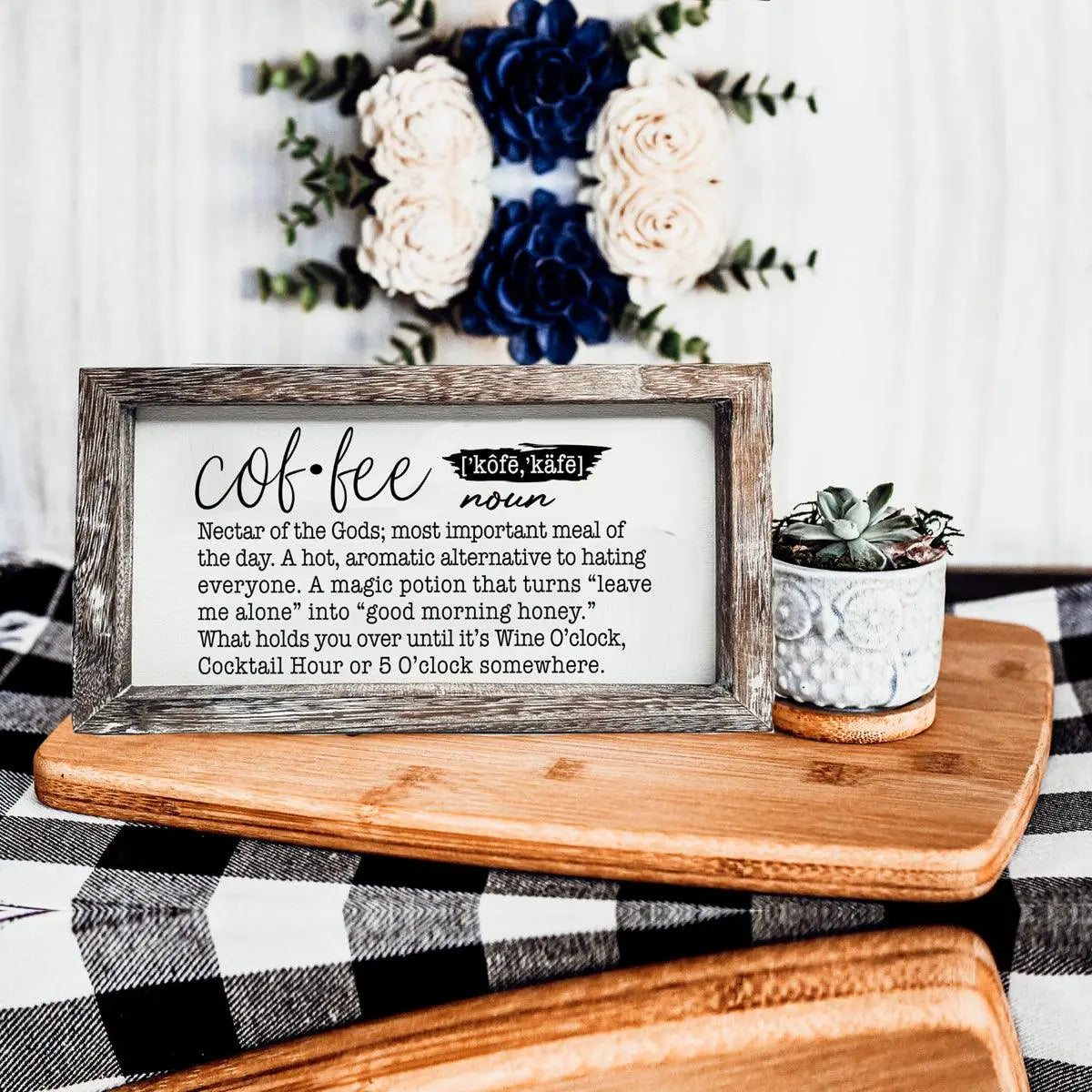 Decorative sign with coffee definition on a wooden surface with flowers in the background
