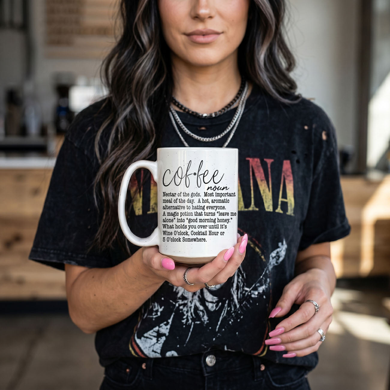 Person holding a mug with 'Coffee' definition text, wearing a black t-shirt with colorful text.