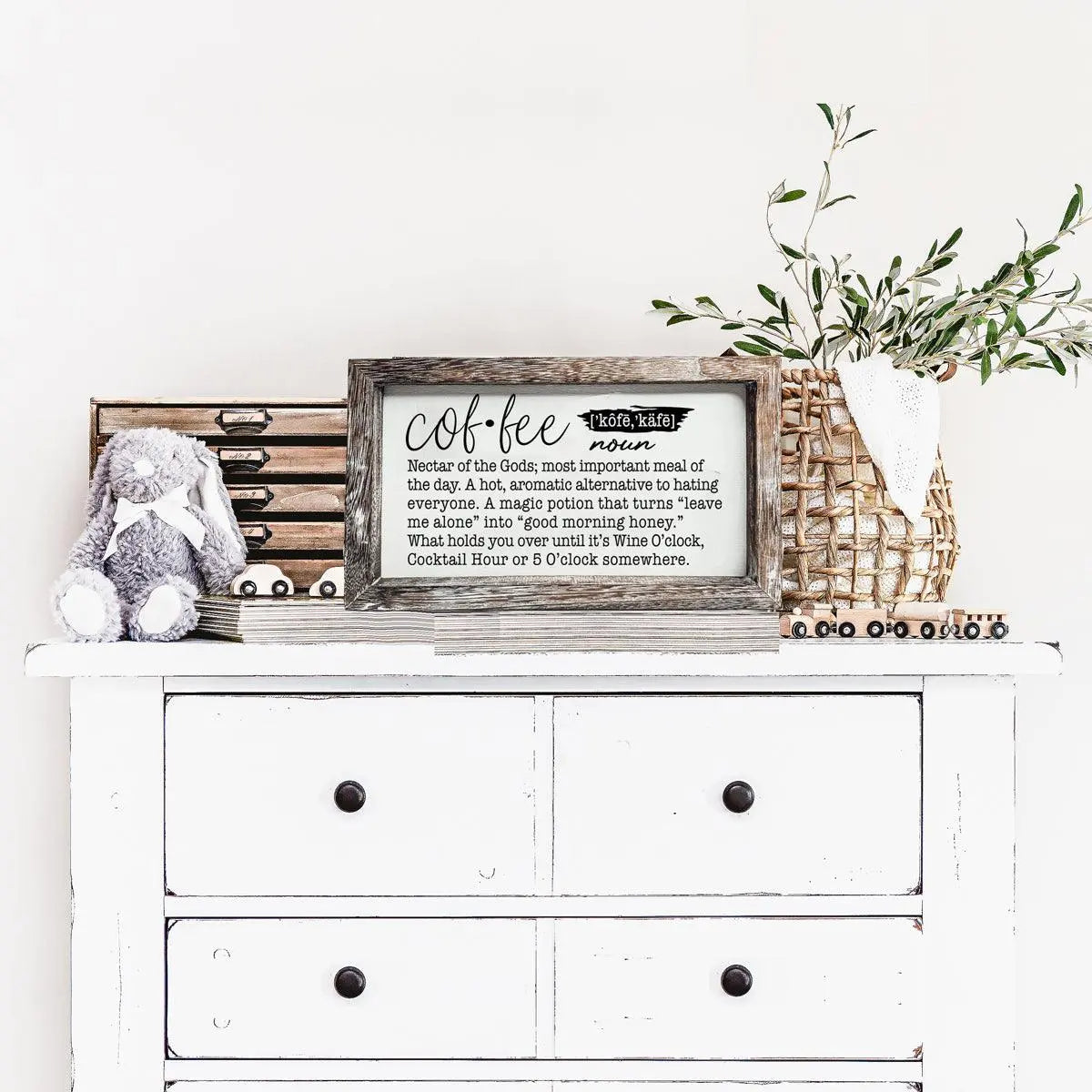 White dresser with decorative items including a framed sign, plush toy, and plant on a white background