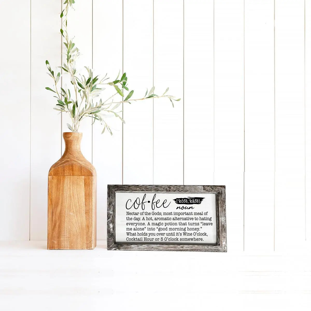 Wooden vase with greenery and framed text on a white wall