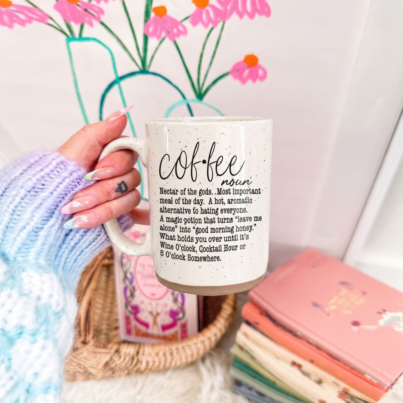 Person holding a mug with 'coffee' definition text, flowers in the background