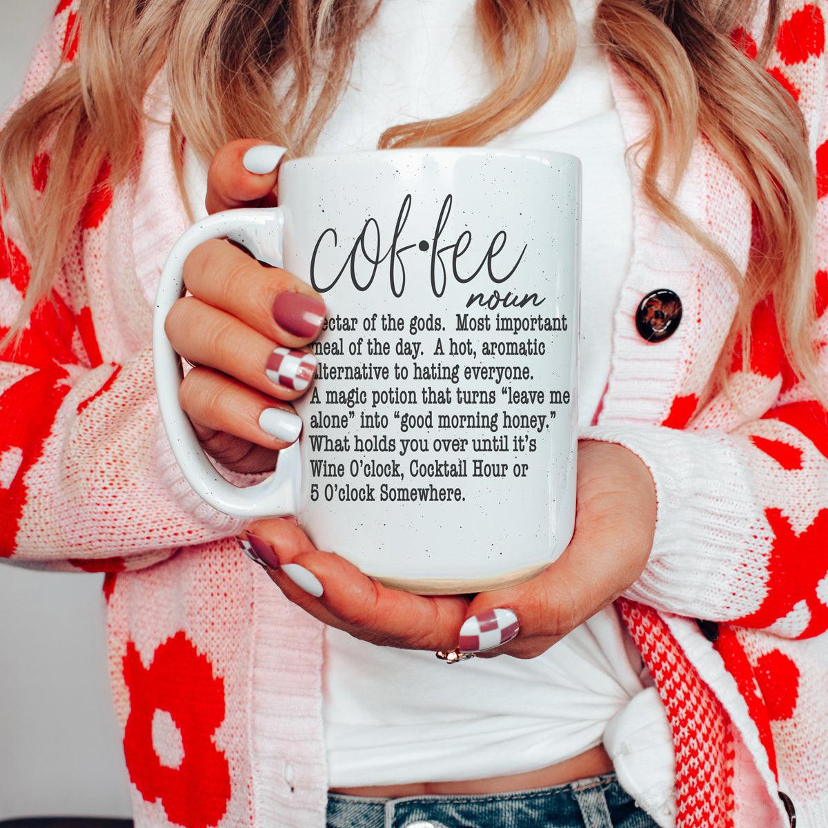 Person holding a mug with a definition of 'coffee' text, wearing a red and white patterned cardigan.