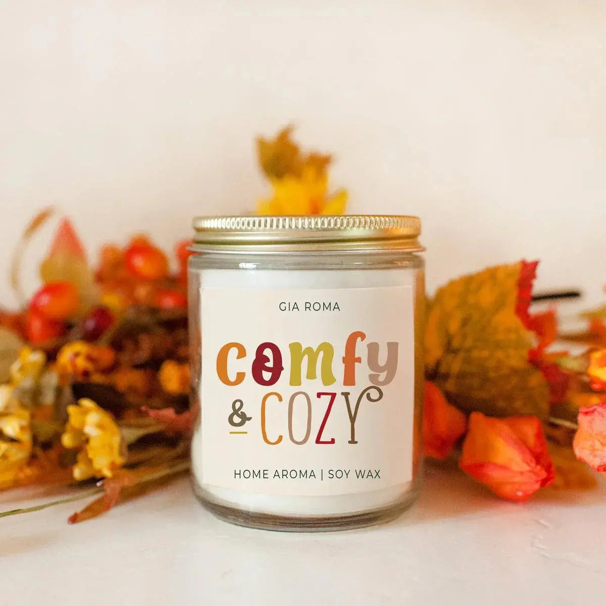 Candle with 'comfy & cozy' label in front of autumn-themed decorations