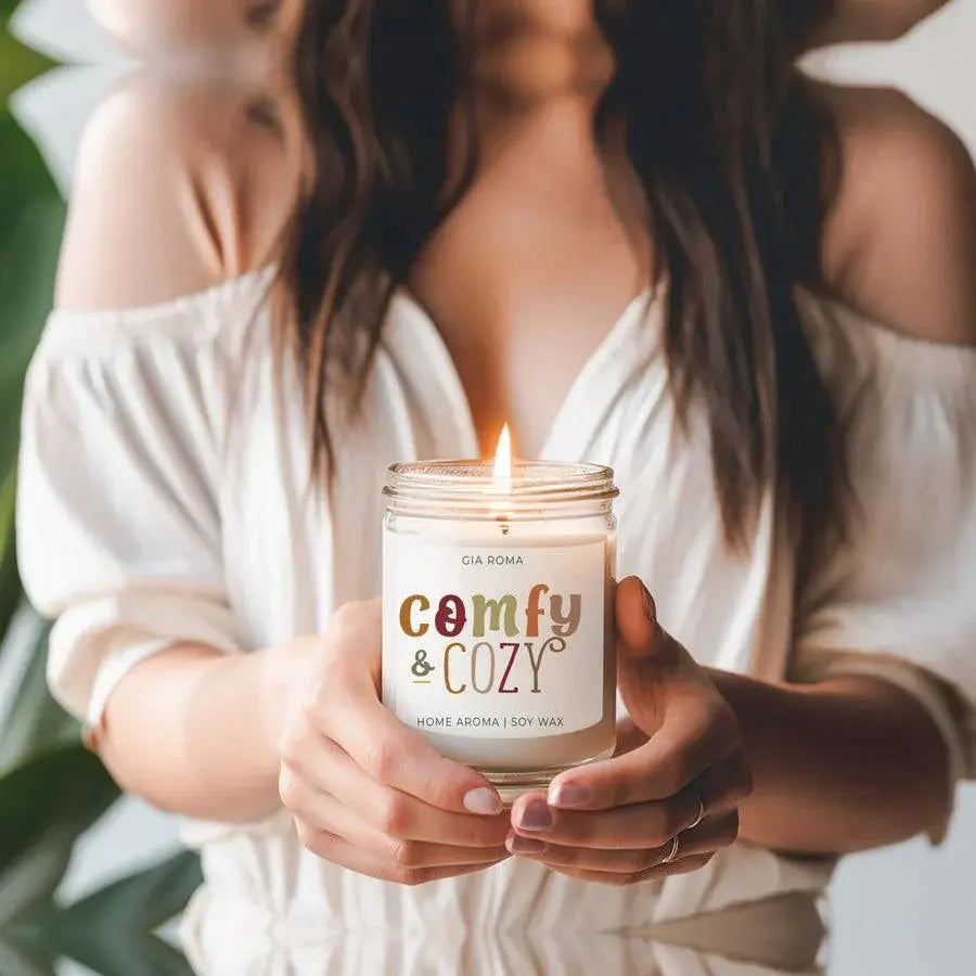 Person holding a 'Comfy & Cozy' candle with a blurred background