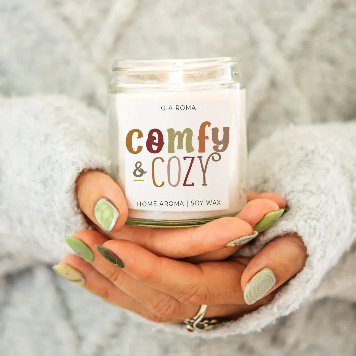 Hand holding a candle labeled 'comfy & cozy' by Gia Roma.