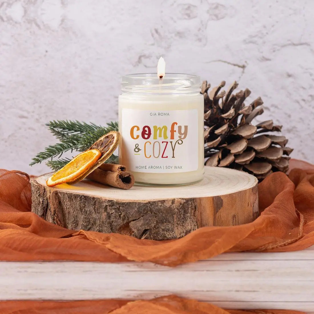 Candle labeled 'Comfy & Cozy' on a wooden stump with decorative elements.