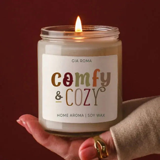 Candle labeled 'Comfy & Cozy' held by a hand with a dark background