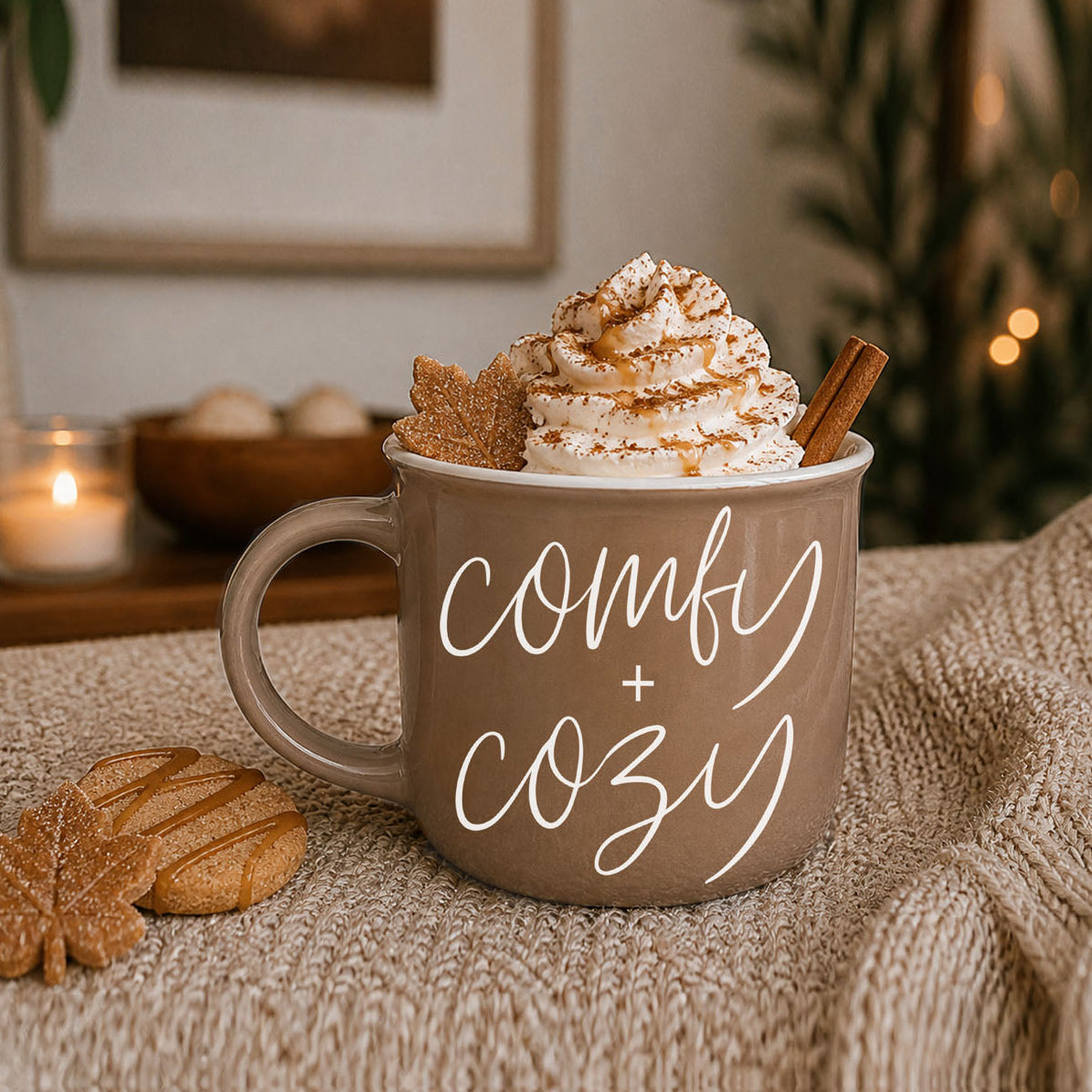 Mug with whipped cream, cookies, and a cinnamon stick on a textured surface with 'comfy + cozy' text.