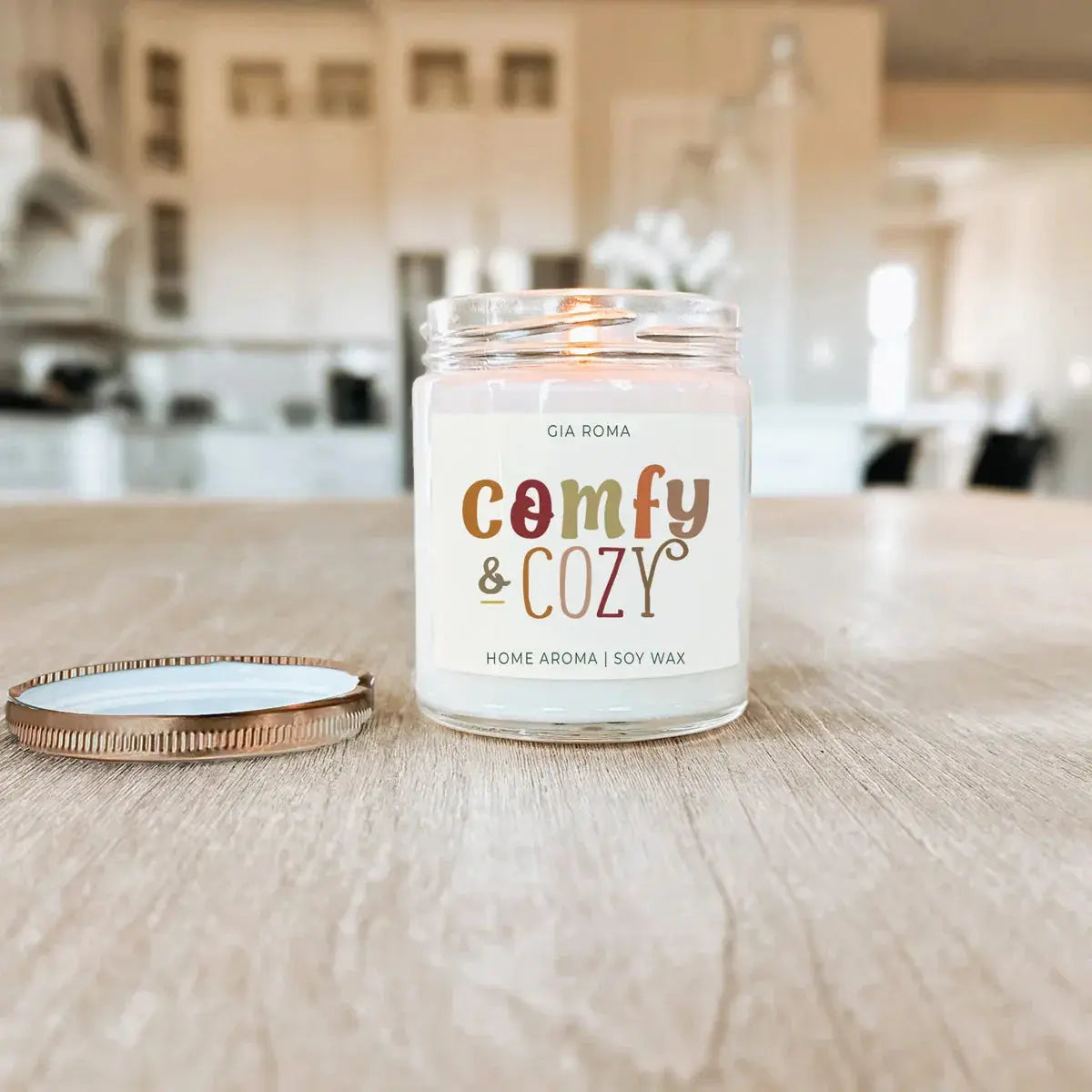 Candle labeled 'comfy & cozy' on a wooden surface with a blurred indoor background