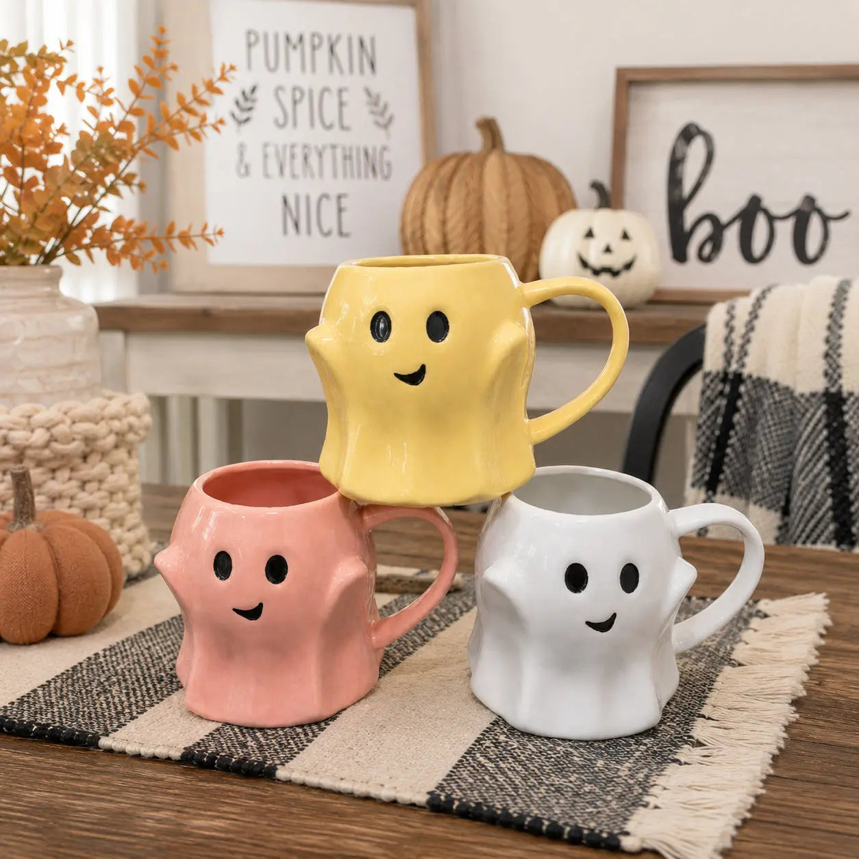 Three colorful mugs with smiley faces on a table with Halloween decorations.