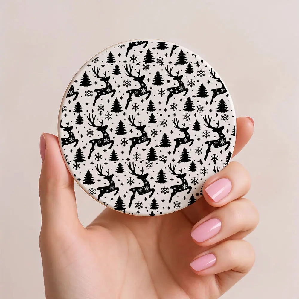 Circular product with deer and tree pattern held by a hand with pink nails on a beige background