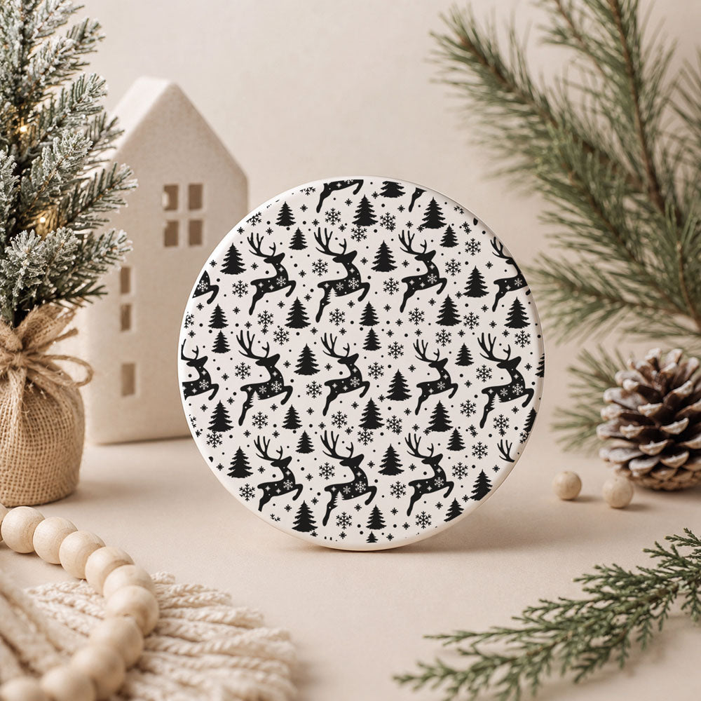 Round decorative item with black deer and tree pattern on a neutral background with Christmas decor.