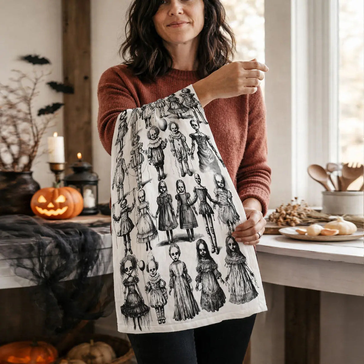 Woman holding a tea towel with black and white pattern in a kitchen setting with Halloween decorations.
