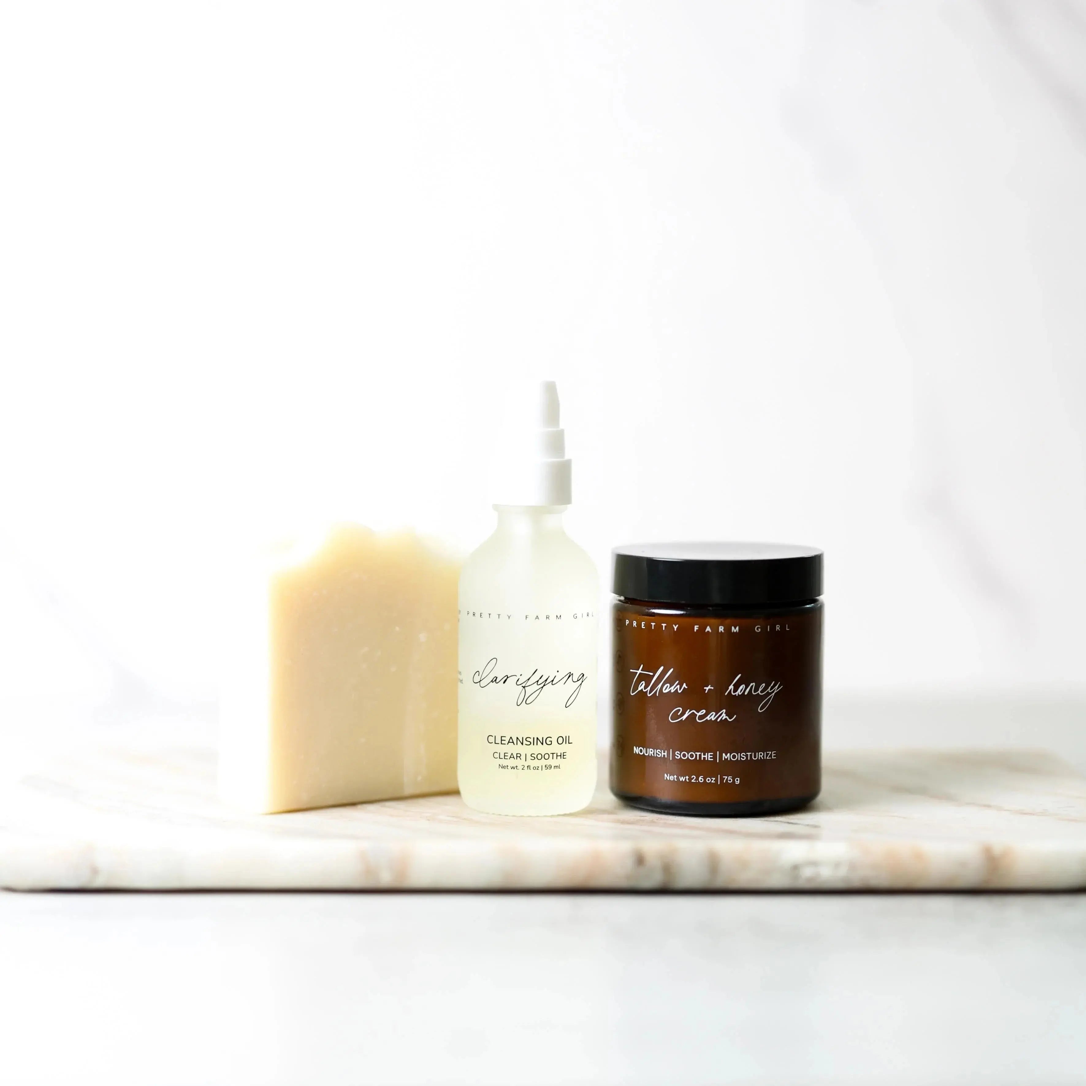 Cozy farmhouse bath essentials: soap, clarifying cleansing oil, and tallow honey cream on marble