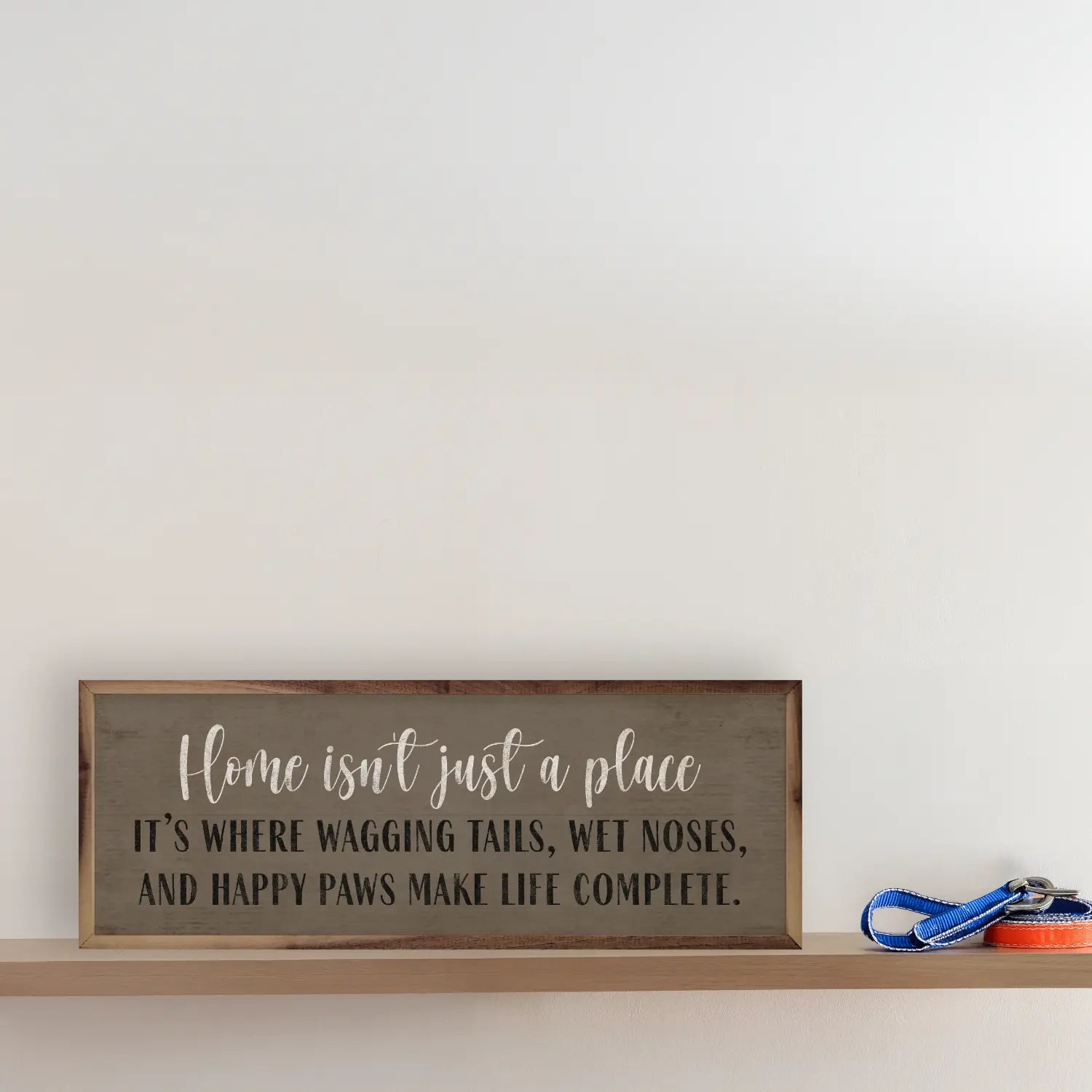 Wooden sign with a quote about home and pets on a shelf against a white wall.
