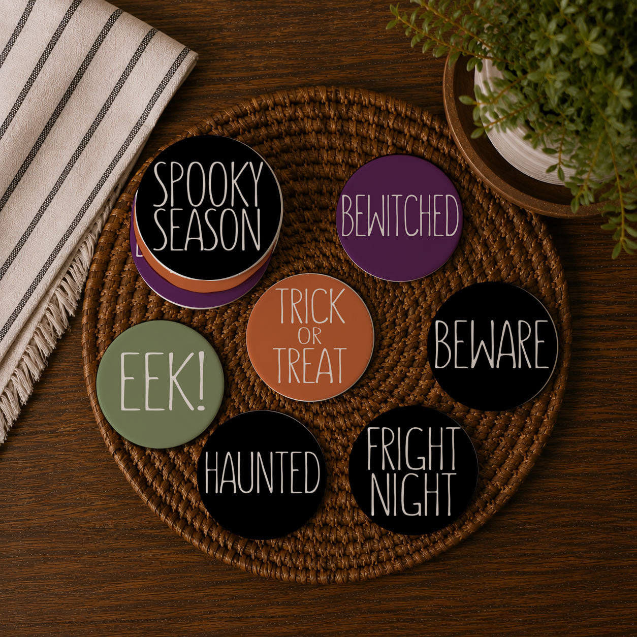 Set of Halloween-themed coasters on a woven mat with a plant and towel in the background.