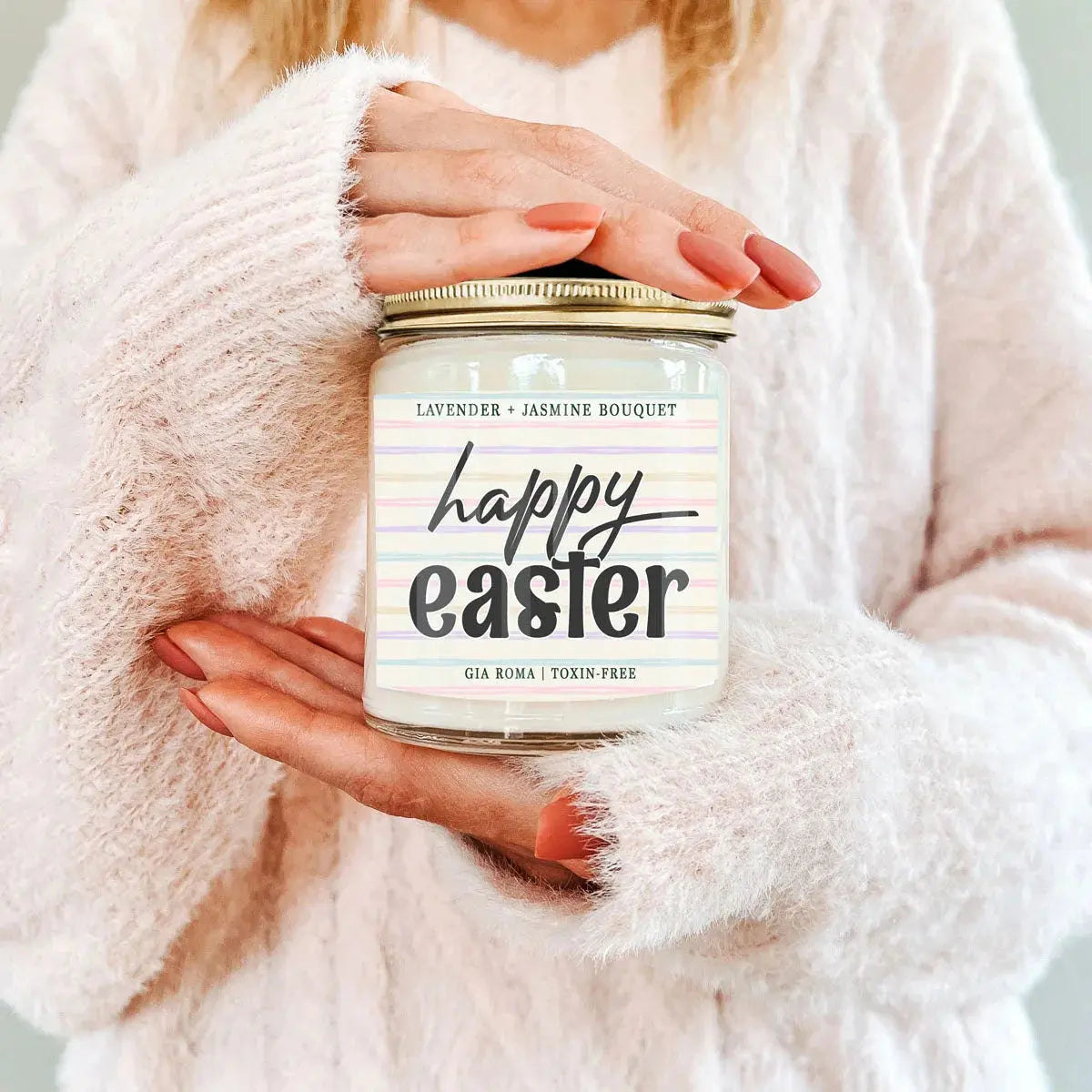 Person holding a 'Happy Easter' candle jar with a soft pink background