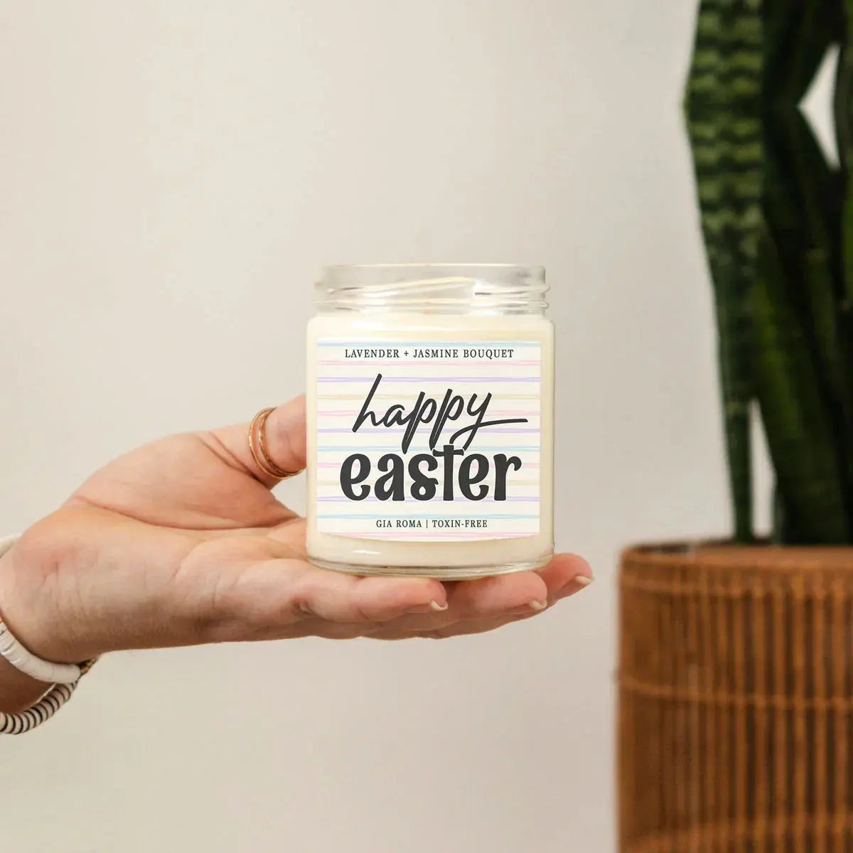 Hand holding a candle labeled 'easter vibes' with a plant in the background