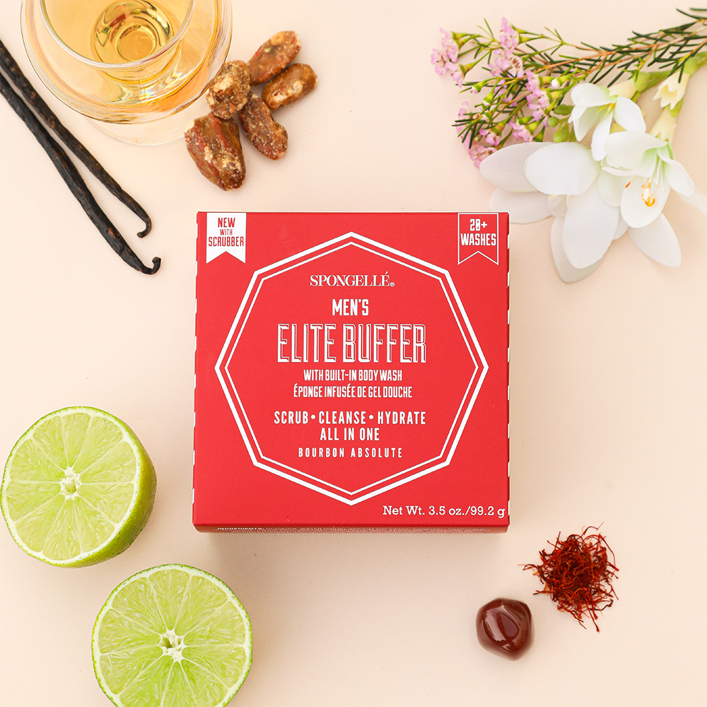 Red box of Men's Elite Buffer by Spongellé on a light surface with limes, flowers, and other items.