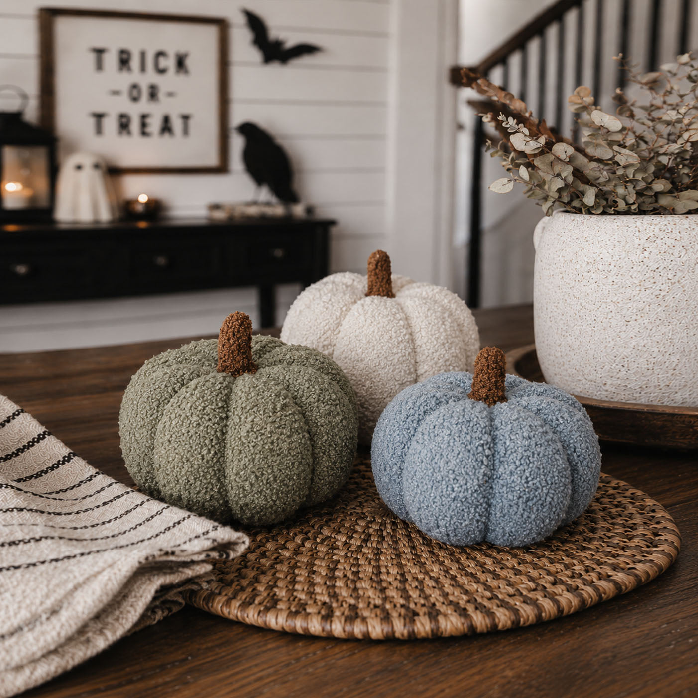 Decorative pumpkins on a woven mat with Halloween-themed decor in the background.