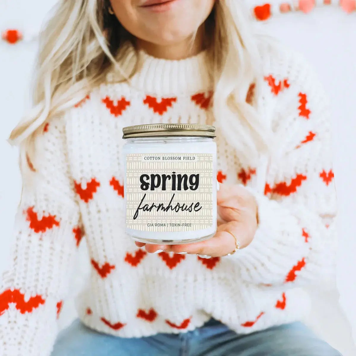Person holding a 'spring farmhouse' candle in a cozy setting