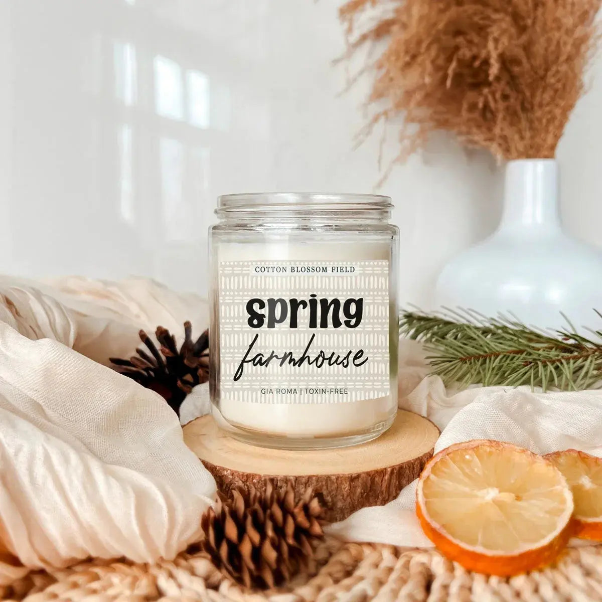 Candle labeled 'Spring Farmhouse' on a wooden coaster with decorative elements.