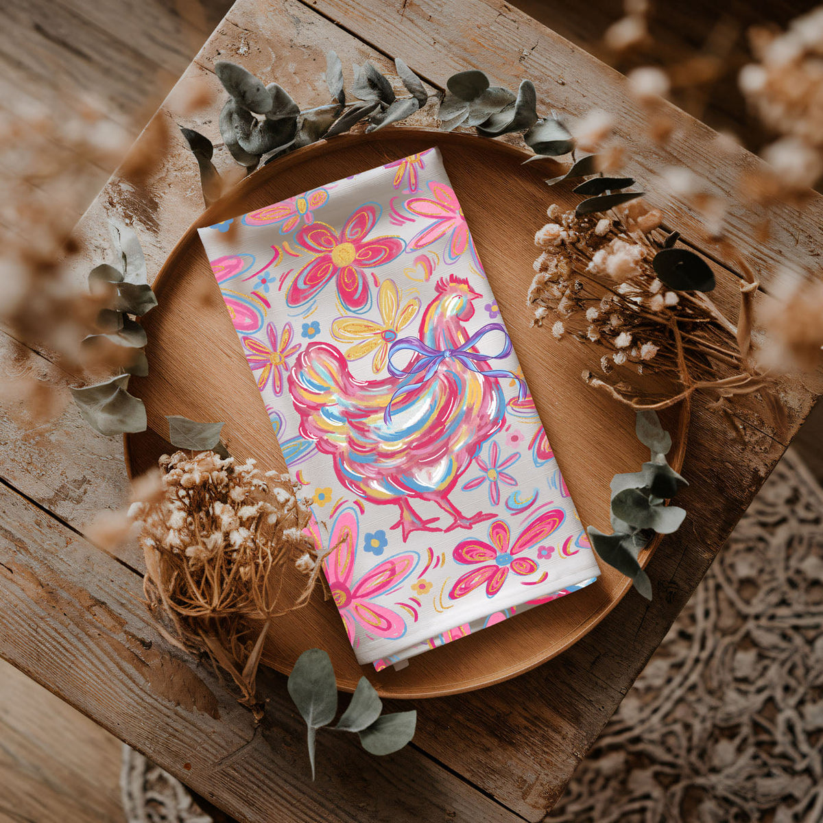 Colorful rooster design on a napkin with dried flowers and leaves on a wooden surface