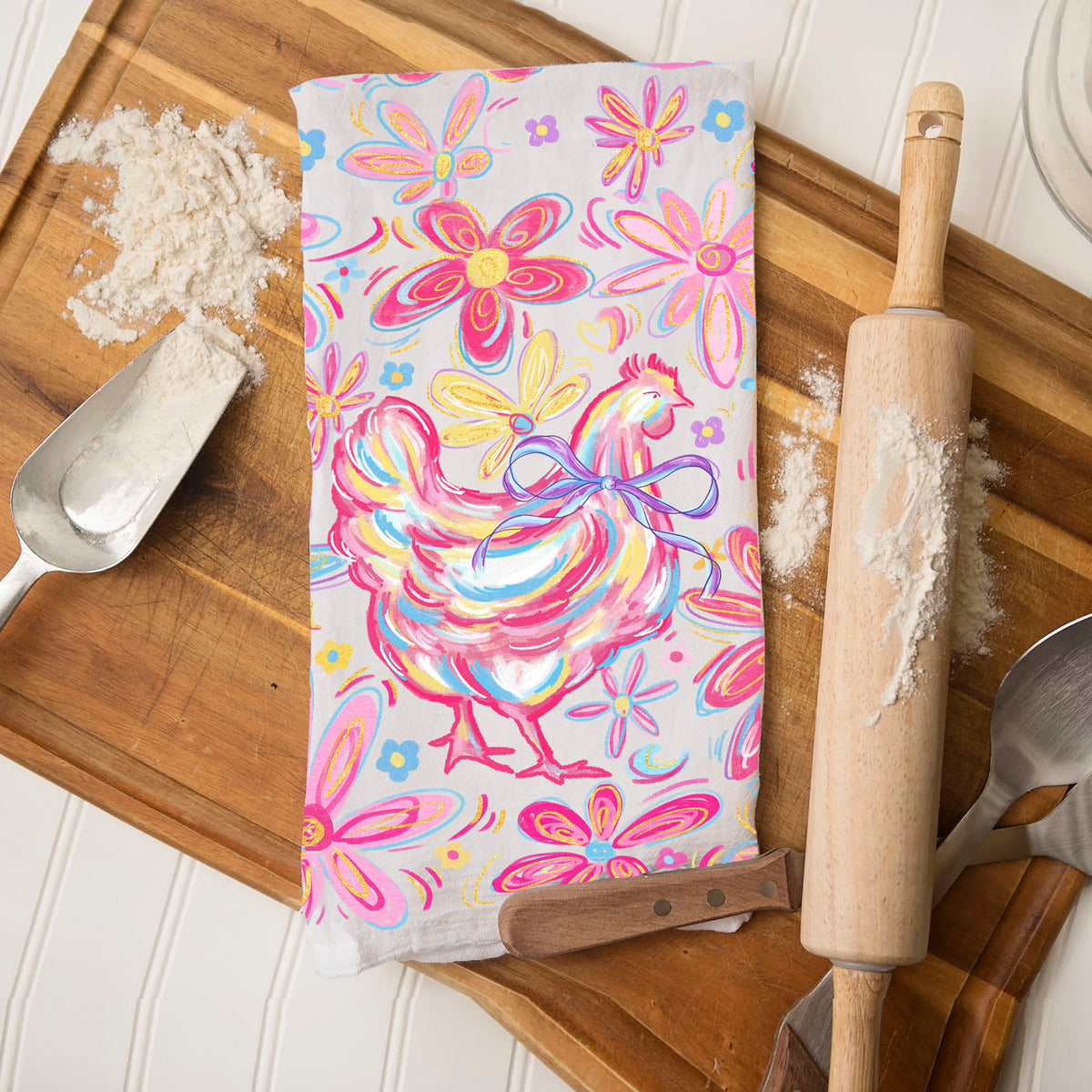 Colorful towel with rooster design on a wooden cutting board with kitchen utensils.