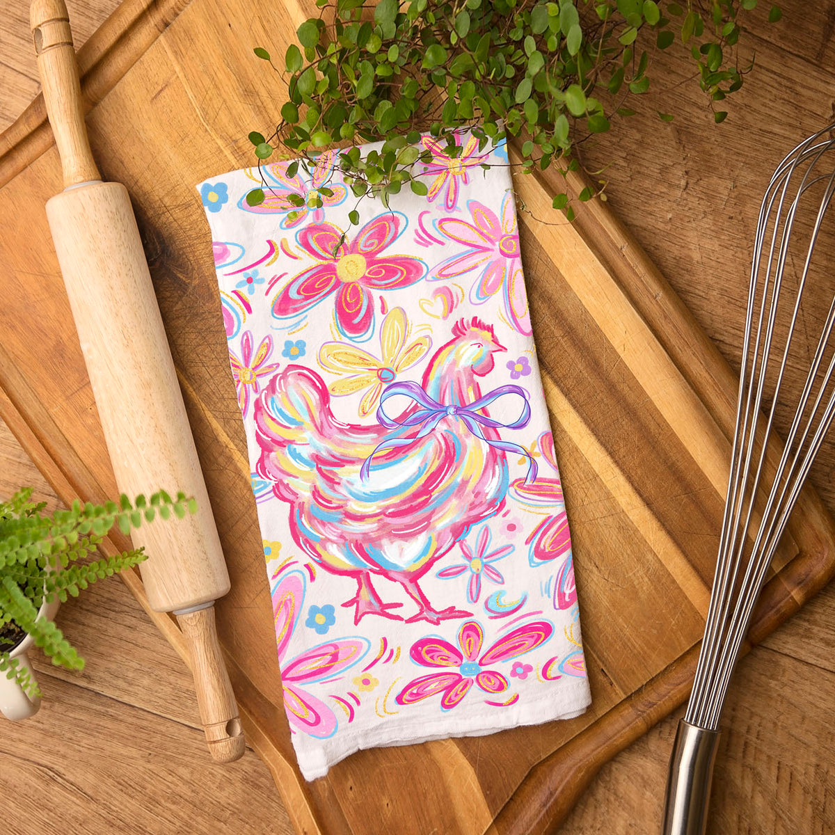 Colorful towel with a chicken design on a wooden surface with kitchen items.