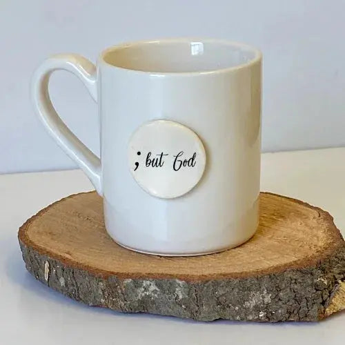 White ceramic mug with '; but God' text on rustic wood slice, cozy farmhouse decor