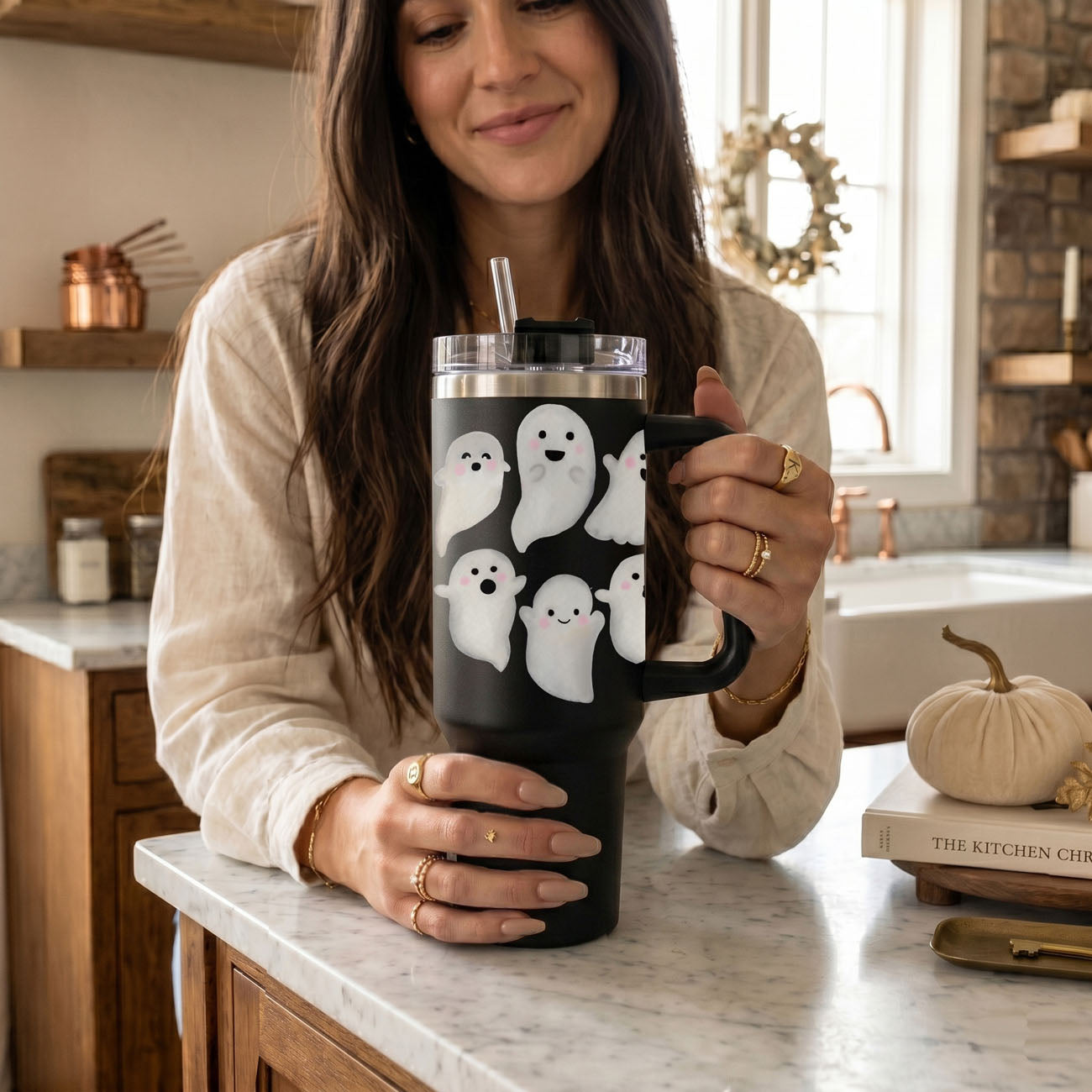 Woman holding a black mug with ghost designs in a kitchen.
