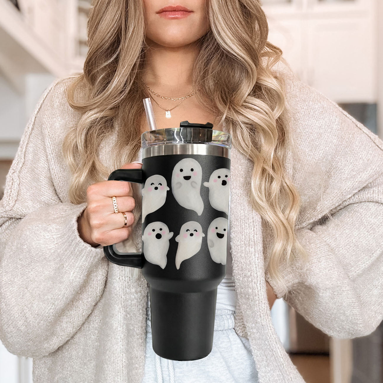 Person holding a black mug with ghost designs, wearing a light gray sweater.
