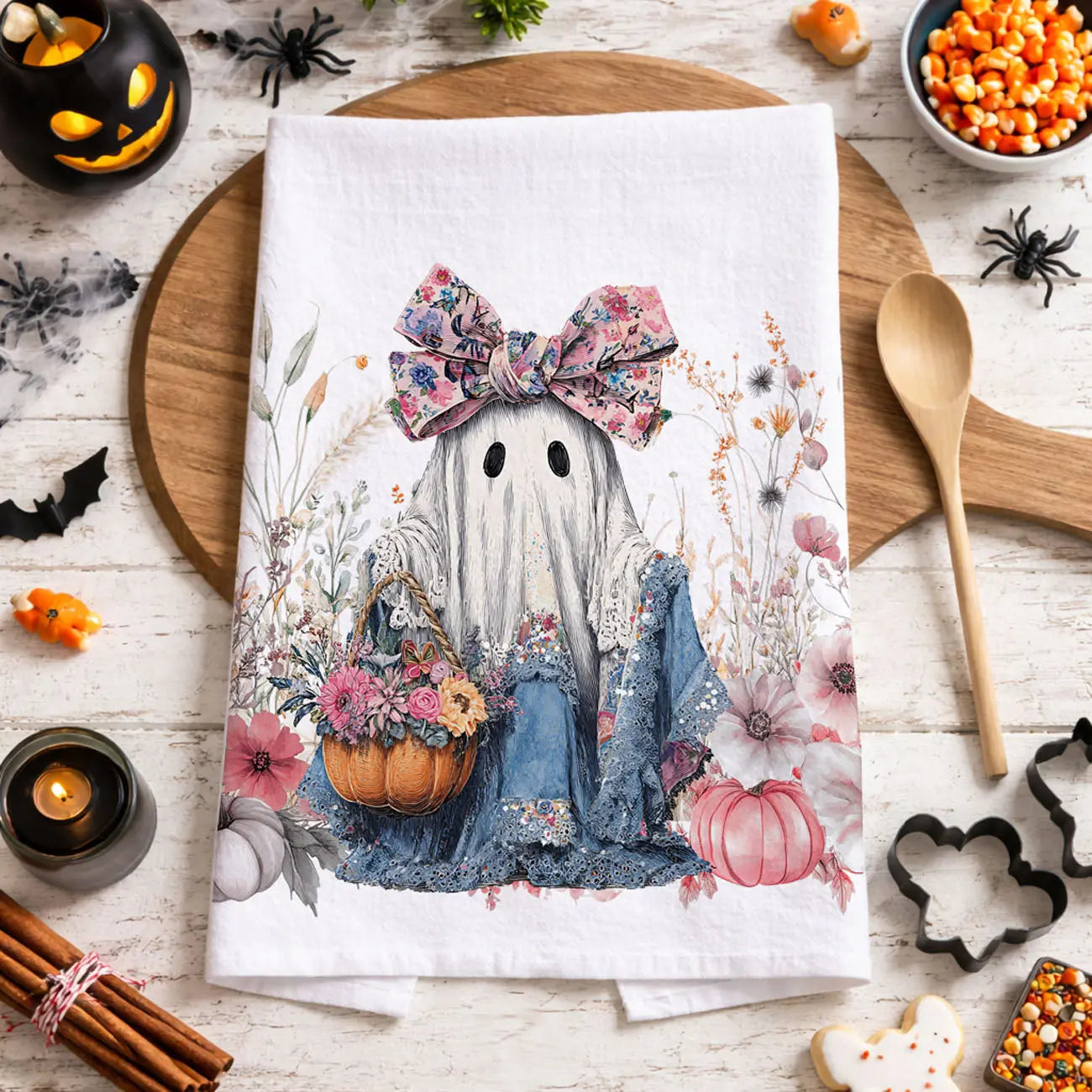 Decorative kitchen towel with a ghost design on a wooden cutting board with Halloween decorations.